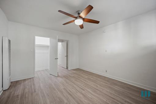 A room with a ceiling fan and light, wooden floors, and white walls.