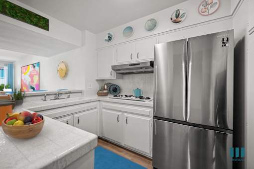 A kitchen with a refrigerator, sink, and a bowl of fruit on the counter.