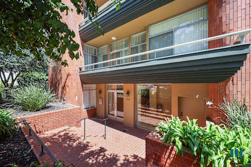 A red brick building with a balcony and a small garden in front.