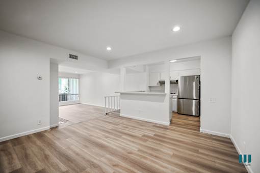 A spacious kitchen with wooden flooring and white walls.