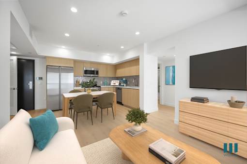 A modern living room with a white sofa, wooden coffee table, and a kitchen area in the background.