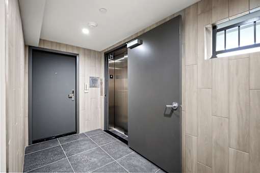 A hallway with a grey elevator and a black door on the left.