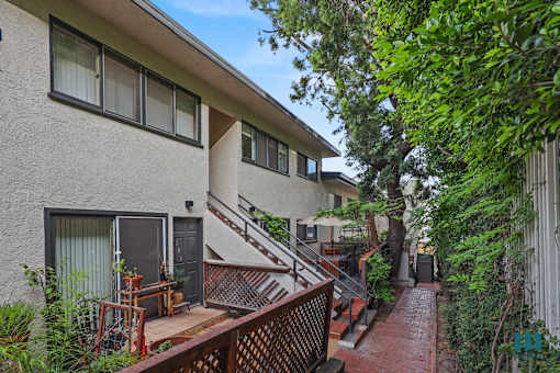 A small patio with a table and chairs is surrounded by a metal fence and trees.