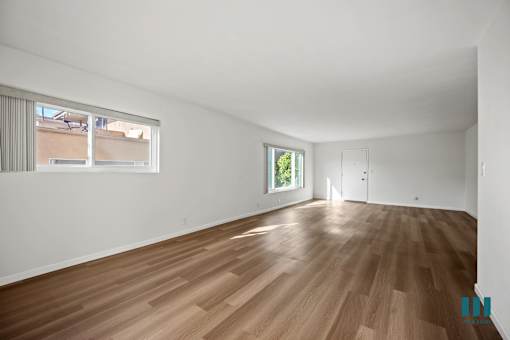 Empty room with wooden flooring and two windows.