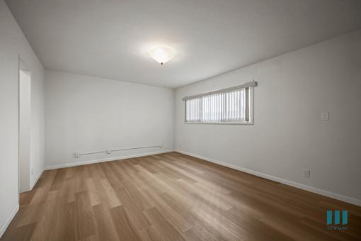 A room with wooden flooring and a window with blinds.
