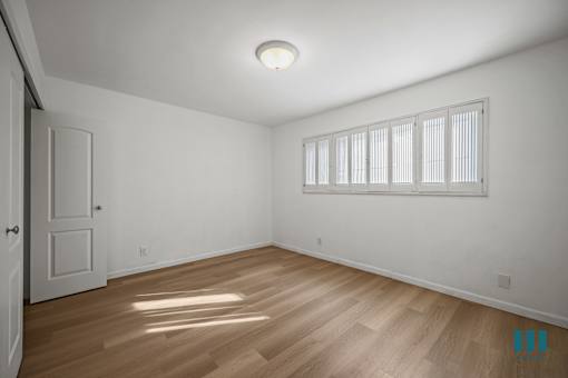 A room with a wooden floor and a window with blinds.