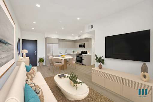 A modern living room with a white sofa, a coffee table, a flat screen TV, and a kitchen area in the background.