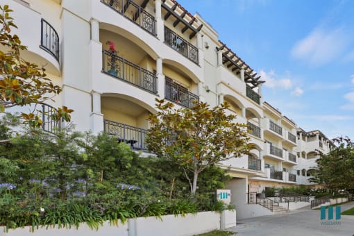 a large white apartment building with trees and a sidewalk
