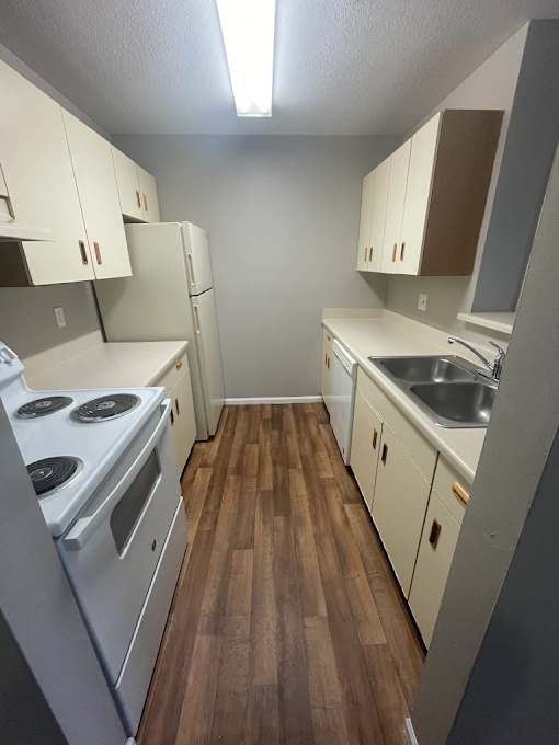 A kitchen with white appliances and wooden floors.
