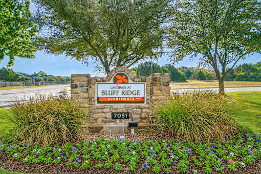 A sign for Bluff Ridge Apartments is surrounded by flowers and greenery.