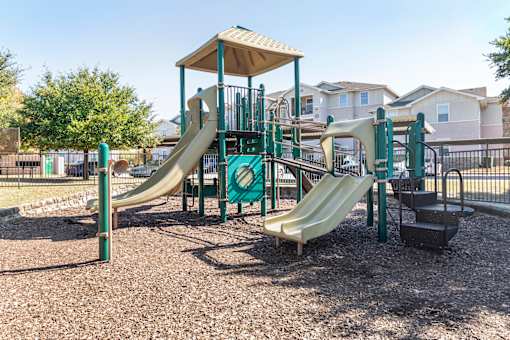 A playground with a green and tan slide and a brown and green play structure.