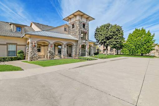 A large house with a stone tower and a driveway in front.