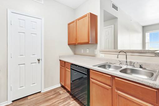 A kitchen with a white door, brown cabinets, and a black dishwasher.