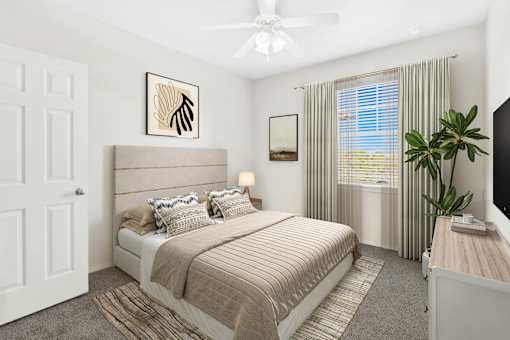 A bedroom with a large bed, a ceiling fan, and a window with curtains.