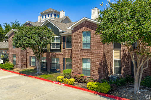 A red brick apartment building with a green tree in front.