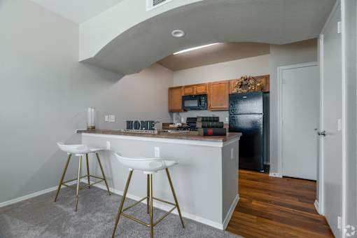 A kitchen with white countertops and gold bar stools.