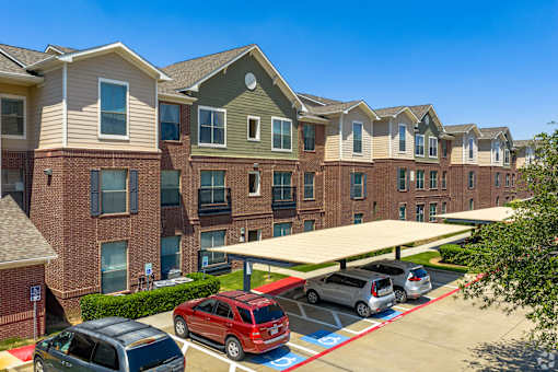 A row of apartment buildings with cars parked in front.