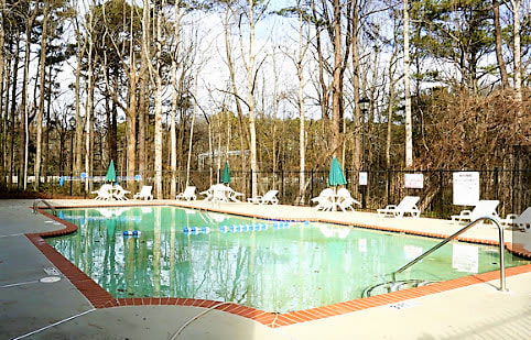 A pool surrounded by trees and chairs at Clarkston Station Apartments, Clarkston, Georgia