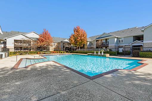 A swimming pool surrounded by a concrete floor and residential buildings.