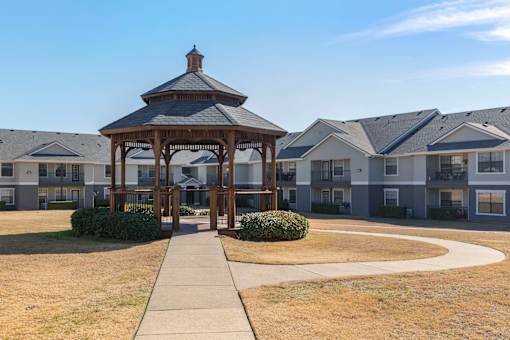 A gazebo is in the middle of a grassy area in front of apartment buildings.