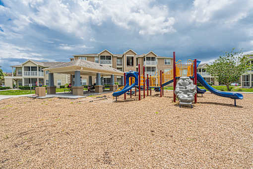 A playground with a slide and a sandbox in front of apartment buildings.