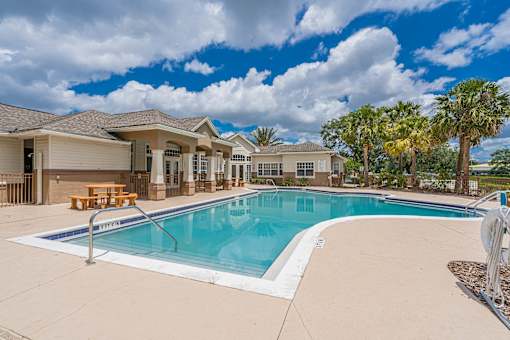 A swimming pool in front of a house with a blue sky and clouds.