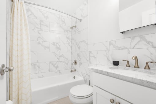 A bathroom with a sink, a mirror, under-cabinet storage, a toilet, and a shower/tub combination with modern tile and hardwood-style flooring.