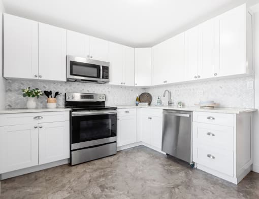 A bright and spacious kitchen with white cabinets, herringbone tile backsplash, stainless steel appliances, and tile-style flooring.