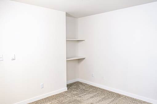 A room with a carpeted floor and a wall-mounted shelf.