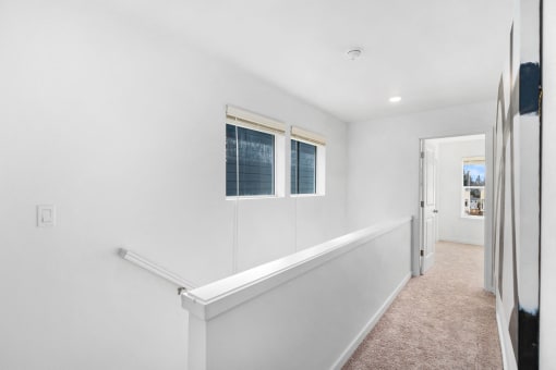 a hallway with white walls and two windows and a white staircase