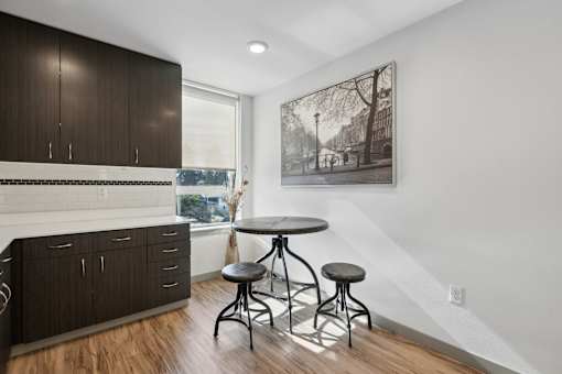 A kitchen with dark wood cabinets and a white backsplash with a bar area and a table with two stools.