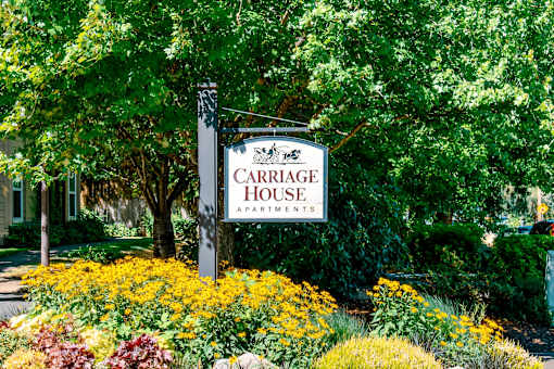 A sign for Carriage House Apartments is surrounded by flowers.