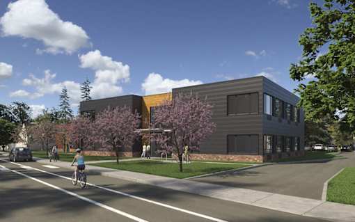A modern building with a grey and yellow facade is surrounded by trees and a clear blue sky.
