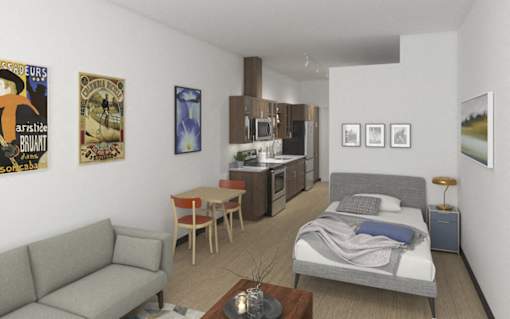 A living room with a grey couch, a coffee table, a bed, and a kitchen area.