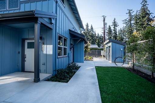 A blue building with a white door and windows is surrounded by greenery.