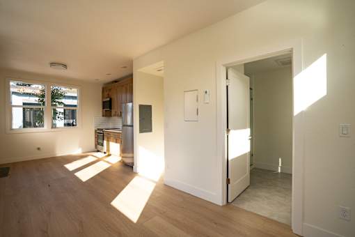 A room with wooden floors and white walls with sunlight coming through the windows.