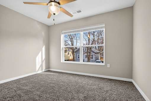 A room with a ceiling fan and a window showing a view of houses.
