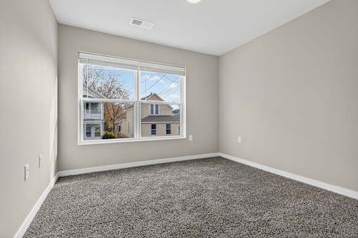 A room with a large window and grey carpet.