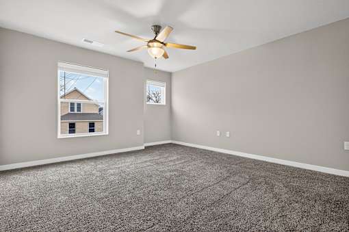 A room with a ceiling fan and a window showing a house.