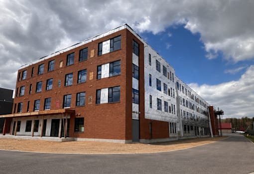 A large, multi-story building with a mix of brick and white exterior walls is under construction.