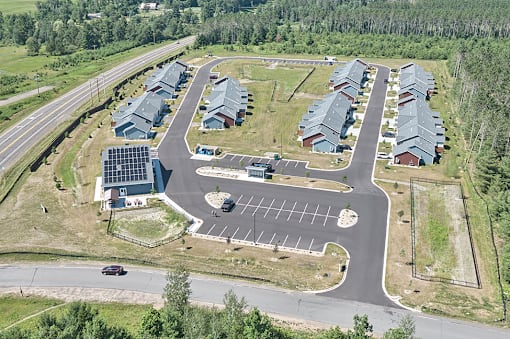 A road with a car driving down it and a parking lot with a building in the background.