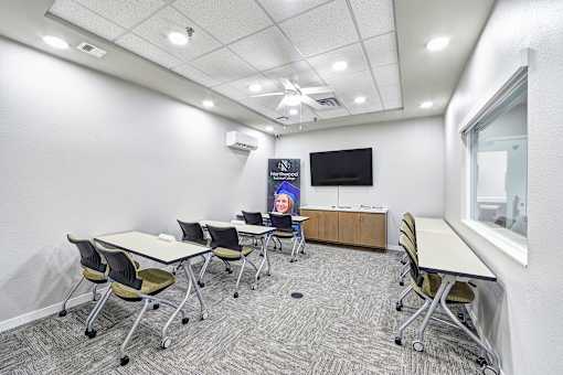 A conference room with a white table, chairs, and a TV screen.