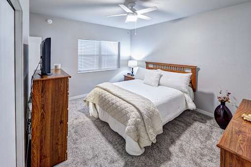 A bedroom with a bed, dresser, and ceiling fan.