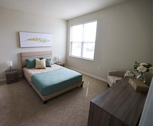 A bedroom with a bed, nightstand, chair, and a painting on the wall.