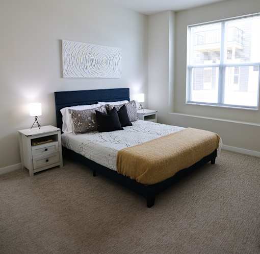 A bedroom with a bed, nightstand, and a painting on the wall.