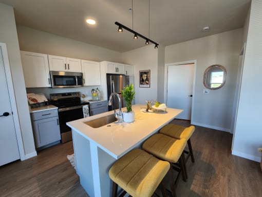 a kitchen with a large island with three stools at The Daniels at Northern Gateway Apartments, Wisconsin