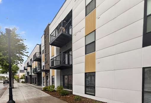A modern apartment building with balconies and a sidewalk in front.