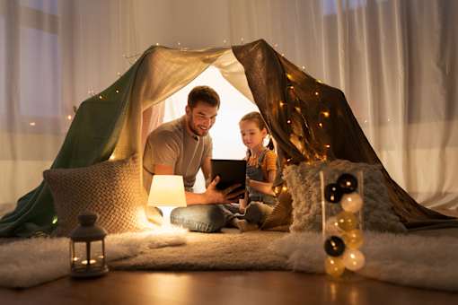 A man and a child are sitting inside a tent-like structure, with the man holding a tablet and the child looking at it.