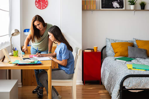 A woman and a girl are sitting at a table with books and papers.