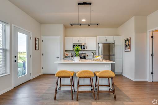 A kitchen with white cabinets and a white island with three stools in front.